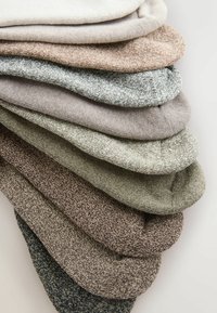 Set aus acht Socken in verschiedenen gedämpften Farben, darunter Beige, Grau, Grün und Braun, mit unterschiedlichen Texturen und Strickmustern.