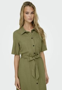 Olive roheline särk-kleit linase sarnase kangaga, millel on lühikesed varrukad, nööpidega esiosa, rinna tasku ja vöökohtade sidumine.