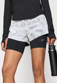 Melnas garās piedurknes tops, kas pārklāts virs pelēkām un baltām rakstotām šortiem. Šortiem ir melns iekšējais oderējums un Nike logo sānos.