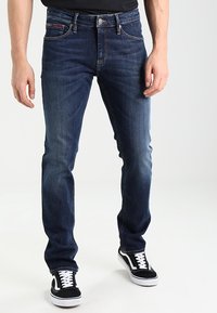 Mörkblå denimjeans med rak passform, som har en femficksdesign och gula sömmar, kombinerat med svarta och vita sneakers.