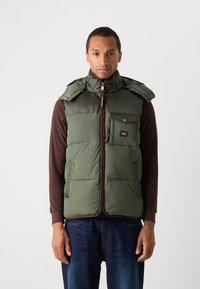 Green padded vest with detachable hood, zip closure, mesh accents, and two side pockets. Worn over a brown long-sleeve shirt.