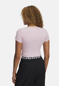 Krátký rukáv, přiléhavý růžový pruhovaný top s kulatým výstřihem. Nosený s černými kalhotami s širokým bílým pasem s logem.