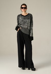 Maglione bianco e nero a pois con scollatura a V e polsini a coste, abbinato a pantaloni neri larghi e scarpe chunky nere con plateau.