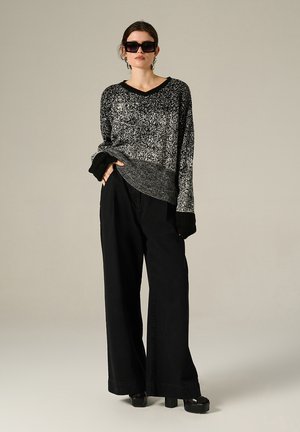Un pull à motifs noir et blanc avec un col en V et des poignets côtelés, associé à un pantalon noir à jambes larges et des chaussures à plateforme noires et épaisses.