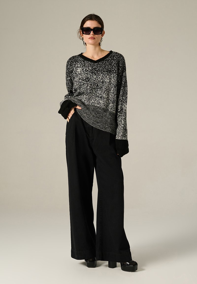 Maglione bianco e nero a pois con scollatura a V e polsini a coste, abbinato a pantaloni neri larghi e scarpe chunky nere con plateau.