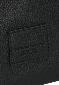Materiale in pelle nera testurizzata con un patch rettangolare con testo in rilievo. La superficie è a granuli con cuciture visibili.