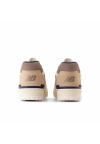 Beige New Balance sneakers with brown suede accents, white sole, and embossed logo. Smooth texture and round shape with cushioned back.