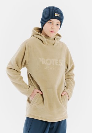 Sweat à capuche en polaire beige clair avec un col montant, des poches avant et un logo discret. Associé à un bonnet côtelé bleu marine.