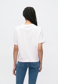 Ροζ ανοιχτόχρωμο κοντομάνικο μπλουζάκι με στρογγυλή λαιμόκοψη, κατασκευασμένο από απαλό ύφασμα· εμφανίζεται από πίσω, σε συνδυασμό με μπλε τζιν.