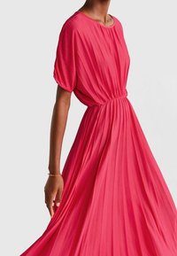 Robe plissée rose avec un col rond et des manches courtes bouffantes. Fabriquée en tissu léger, elle possède une taille élastique pour un ajustement fluide.