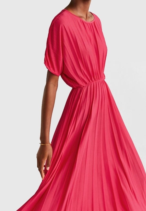 Robe plissée rose avec un col rond et des manches courtes bouffantes. Fabriquée en tissu léger, elle possède une taille élastique pour un ajustement fluide.