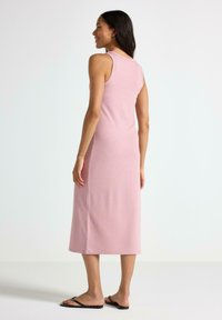 Lys pink ribbet midi kjole med en tætsiddende silhuet, ærmeløs design, sideslids og en glat tekstur. Kombineret med tynde sorte sandaler.