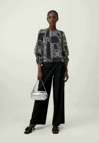 Sorte vide benbukser parret med en marineblå mønstret bluse med puffede ærmer. En metallisk håndtaske tilføjer kontrast i farve og tekstur.