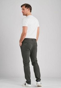 Sive hlače s slim fit krojem, z bočnimi in zadnjimi žepi, v kombinaciji s prilegnjeno belo majico in belimi športnimi copati.