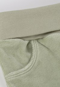 Light green fabric featuring a soft texture with a ribbed knitted waistband. Includes a front pocket and subtle stitching details.
