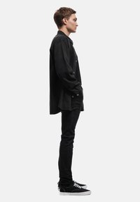 Camisa de mezclilla negra con botones, corte holgado y dobladillo redondeado. Combinada con jeans negros ajustados y zapatillas negras con detalles blancos.