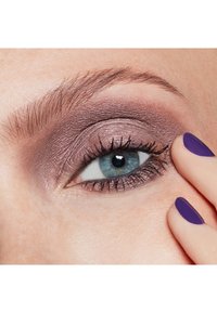 Gros plan sur un œil avec un fard à paupières violet et du mascara, accompagné d'une main avec un vernis à ongles violet sur un seul ongle, mettant en valeur les détails et la texture.