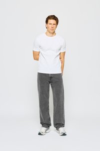 Camiseta blanca de manga corta, jeans grises de corte holgado y zapatillas blancas con acentos azules. El atuendo tiene una apariencia casual y cómoda.