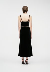 Μαύρο βελούδινο φόρεμα με δαντελένιες λε�πτομέρειες στη μέση και τις τιράντες. Μεσαίου μήκους, εφαρμοστό μπούστο, ρέουσα φούστα και μινιμαλιστικός σχεδιασμός.