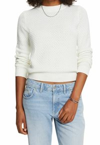 Un pull en tricot blanc avec un motif texturé, des manches longues et un col rond. Associé à un jean en denim bleu clair.
