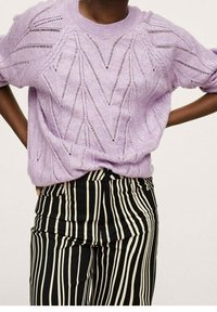 Pull en maille lavande avec un motif ajouré, associé à un pantalon taille haute noir et blanc à rayures, à coupe décontractée.