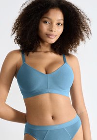 Lyseblå trådløs bh lavet af glat stof, med brede stropper og et enkelt, sømløst design. Logo vist på båndet.