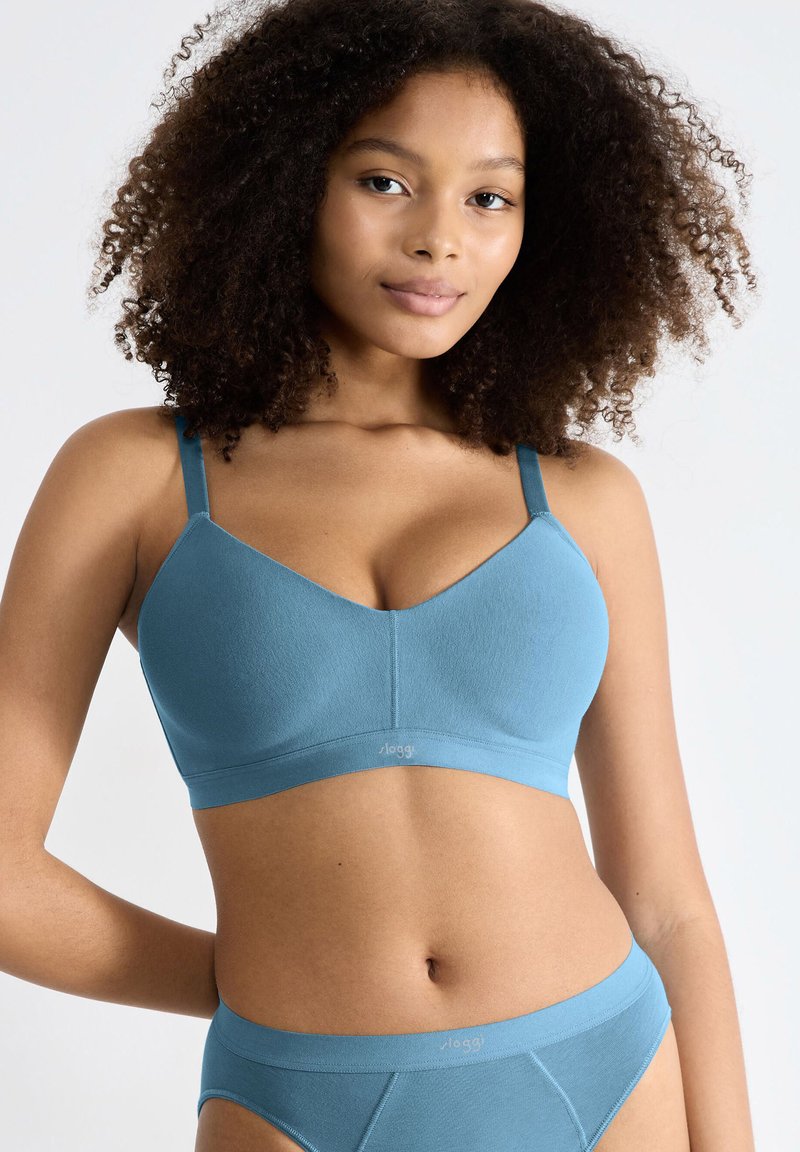 Lyseblå trådløs bh lavet af glat stof, med brede stropper og et enkelt, sømløst design. Logo vist på båndet.