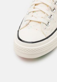 Sneakers z płótna w kolorze kremowym z kolorowymi plamkami. Okrągły czubek z gumową osłoną i czarnym wykończeniem. Teksturowana gumowa podeszwa z diamentowym wzorem.