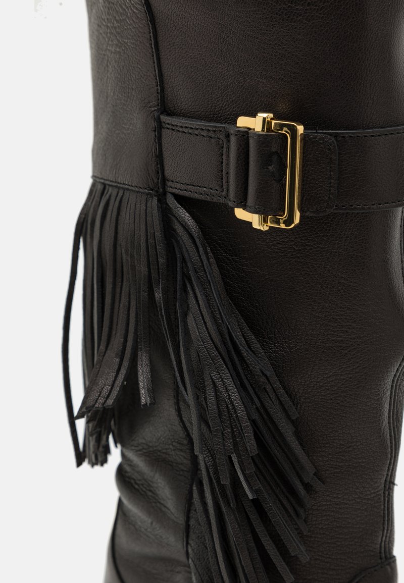 Black leather knee-high boot with a textured finish, featuring long leather fringes and a gold-tone metal buckle accent.