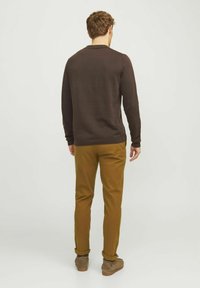 Pull marron à manches longues avec un col rond, associé à un pantalon skinny de couleur moutarde et des bottines grises à la cheville. Texture lisse, coupe décontractée.