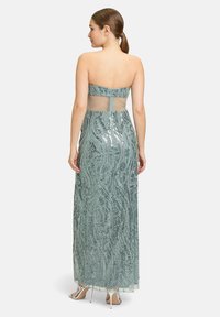 Lange, strapless avondjurk in licht teal met een doorschijnende achterkant. Bevat intricates pailletten detail in golvende patronen, met een vloerlange uitstraling.