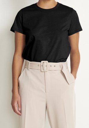 Person iført en ensfarvet sort t-shirt med korte ærmer, stukket ned i beige bukser med høj talje, med et matchende bælte og rektangulært spænde.