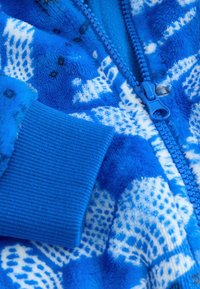 Jacket din polar albastru cu un model texturat și accente albe contrastante. Include un fermoar albastru și mansete cu rifluri la mâneci.