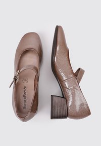 Zapatos Mary Jane de cuero marrón con punta redondeada y correa, que cuentan con un acabado texturizado y un tacón cuadrado y ancho.