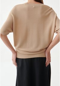 Top in maglia beige con maniche corte e vestibilità morbida, caratterizzata da un orlo a coste. Indossato sopra una gonna nera, mostra una texture liscia e una silhouette elegante.