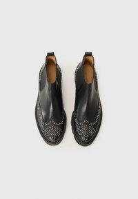 Botas de tobillo de cuero negro con punta redonda, acentos decorativos de tachuelas, paneles laterales elásticos y suela texturizada.