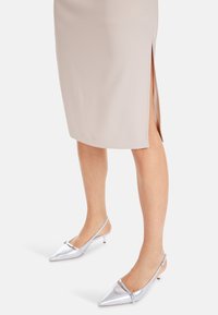 Beige kokerrok met een zijspleet, gecombineerd met zilveren satijnen slingback hakken met een spitse neus en een kleine stilettohak.