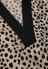 Tkanina w wzór lamparta z beżowym tłem i czarnymi oraz brązowymi plamami. Wyraźny czarny elastyczny wykończenie przy dekolcie w kształcie litery V. Miękka tekstura.