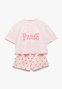 Gekürztes pinkes Baumwoll-T-Shirt mit "PARIS" in gemusterten Buchstaben, kombiniert mit gestreiften Shorts mit roten Herz-Akzenten auf einem hellen Hintergrund.