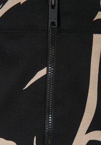 Gros plan sur une fermeture éclair noire sur un tissu avec des formes abstraites beige, tirette marquée de la marque DKNY.