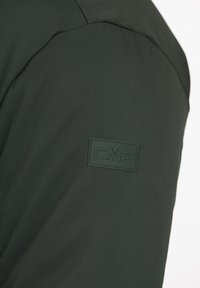 Mørkegrøn jakkestof med glat tekstur, udstyret med et gummibelagt CMP-logo-patch på overarmen, skråtstillet for at fremhæve detaljerne.