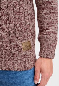 Pull en tricot marron et beige, présentant un motif en relief. Inclus une étiquette texturée "Solid" à l'avant. Coupe décontractée avec des manches côtelées.