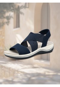 Navy blue sandal with cross-strap design, made of breathable mesh material. Thick white sole with textured accents for grip.