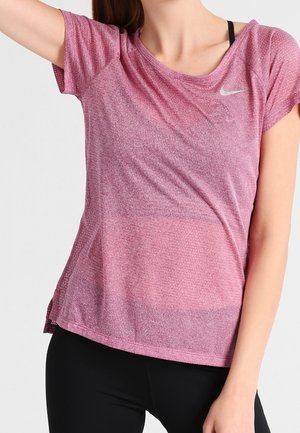 Kvinde iført en kortærmet, lys lilla Nike træningsshirt med sorte sports-bh-stropper synlige, kombineret med sorte leggings.