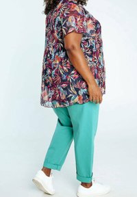 Haut à imprimé floral avec manches courtes dans des couleurs foncées, associé à un pantalon turquoise ample. Comprend des poignets retroussés et des baskets blanches.