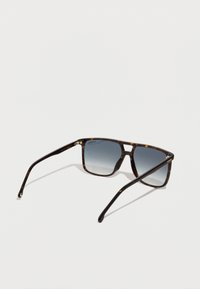 Gafas de sol carey con lentes oscuros degradados. Forma cuadrada, varillas delgadas y un logo sutil en la patilla. Material de plástico suave.