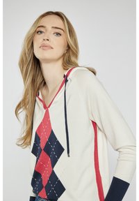 Kapturowa bluza w kolorze kremowym z czerwonym i granatowym wzorem argyle, długimi rękawami i detalem ze sznurkiem przy dekolcie. Miękka faktura.