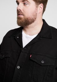 Black denim jacket with a button-up front, two chest pockets, and a collar. Features sturdy stitching and a small red Levi's logo accent.