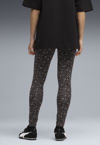 Leggings neri con stampa leopardata, dalla texture liscia, forma aderente e una leggera lucentezza, abbinate a scarpe da ginnastica nere.