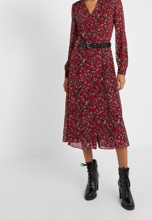 Mujer con un vestido midi rojo con flores, de manga larga, cinturón negro en la cintura y botines negros con cordones y tacón.